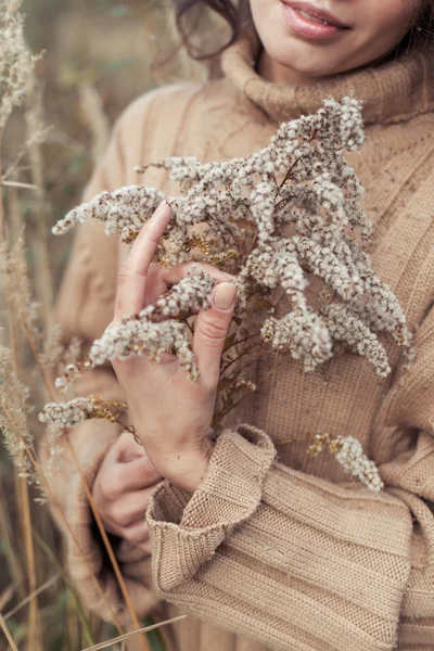Beautiful sad cute attractive woman in a beige sweater wide in a field of dry grass on a cold autumn cloudy day, holding a dry branch, a photo in a beige and coffee tones, chocolate hues — Stock Photo, Image