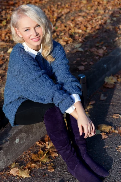 Beautiful cute blonde girl in a blue jacket sitting on the road in the autumn Park — Stock Photo, Image