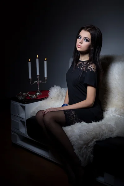 Belle fille douce sexy avec lèvres pleines maquillage lumineux assis sur le canapé avec un verre de vin dans une robe de soirée noire — Photo