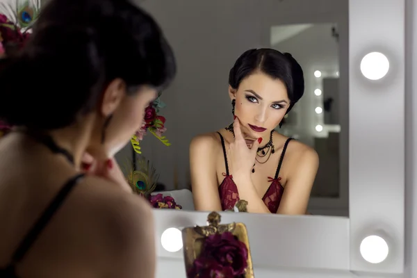 Красивая сексуальная молодая женщина выставляет напоказ перед зеркалом в гримерке в кружевном белье в стиле ретро с ярким макияжем и красивыми вечерними прическами, снятыми в стиле 20-х годов — стоковое фото