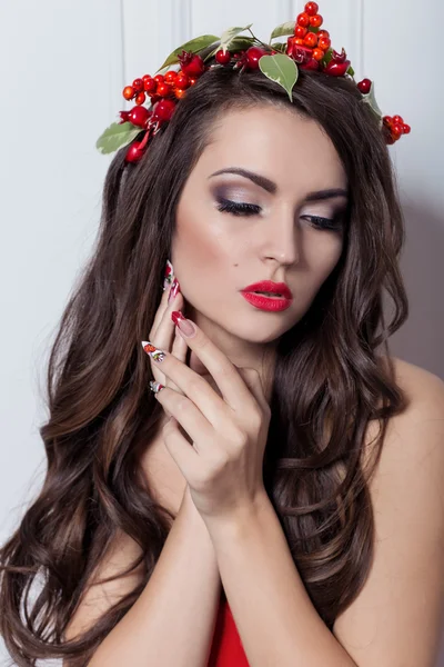 Noël élégante femme de mode. Coiffure et maquillage du Nouvel An de Noël. Magnifique style Vogue Dame avec des décorations de Noël sur la tête, boules, maquillage professionnel, rouge à lèvres rouge longue robe de soirée rouge — Photo