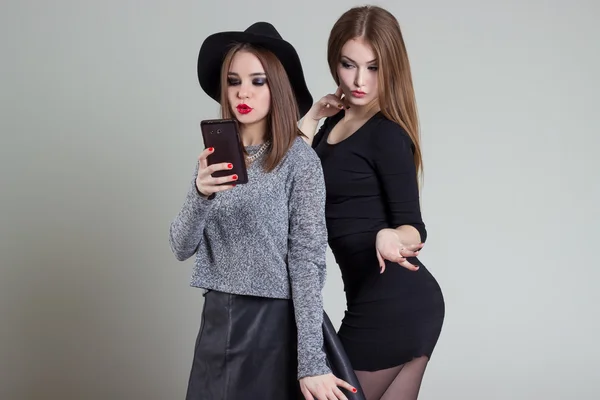 Two cheerful smiling sexy girl girlfriends photographed on the phone, do selfie phone in the studio on a gray background — Stock Photo, Image