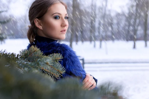 Piękna sexy kobieta ładny w niebieski płaszcz z jasny makijaż stojącego obok choinki w śniegu — Zdjęcie stockowe