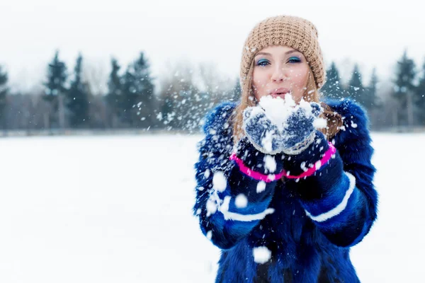Vacker söt sexig lekfull glad ung kvinna i blå jacka i den gemensamma jordbrukspolitiken spelar med snö i parken — Stockfoto