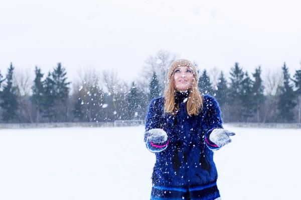 Hermosa linda sexy juguetona feliz joven con un abrigo azul en la gorra jugando con la nieve en el parque — Foto de Stock