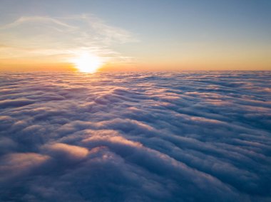 Kıvırcık bulutların üzerinde gün batımı, havada yüksek uçuş. Güneşin son ışınları bulutların üzerinde parlıyor.