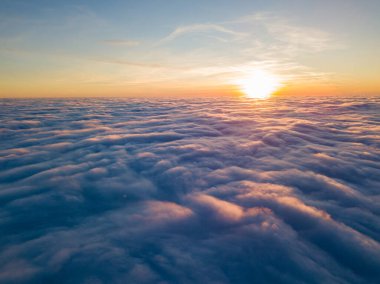 Kıvırcık bulutların üzerinde gün batımı, havada yüksek uçuş. Güneşin son ışınları bulutların üzerinde parlıyor.
