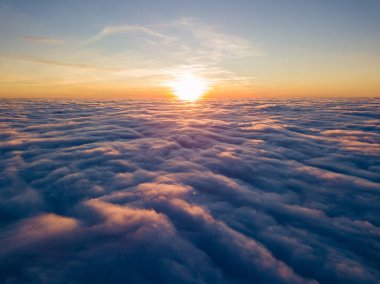 Kıvırcık bulutların üzerinde gün batımı, havada yüksek uçuş. Güneşin son ışınları bulutların üzerinde parlıyor.