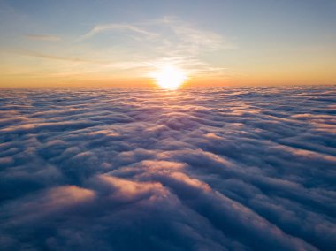 Kıvırcık bulutların üzerinde gün batımı, havada yüksek uçuş. Güneşin son ışınları bulutların üzerinde parlıyor.