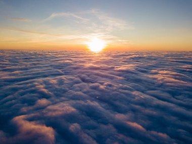 Kıvırcık bulutların üzerinde gün batımı, havada yüksek uçuş. Güneşin son ışınları bulutların üzerinde parlıyor.
