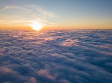 Kıvırcık bulutların üzerinde gün batımı, havada yüksek uçuş. Güneşin son ışınları bulutların üzerinde parlıyor.