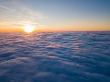 Kıvırcık bulutların üzerinde gün batımı, havada yüksek uçuş. Güneşin son ışınları bulutların üzerinde parlıyor.