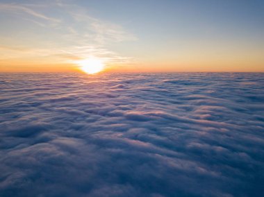 Kıvırcık bulutların üzerinde gün batımı, havada yüksek uçuş. Güneşin son ışınları bulutların üzerinde parlıyor.