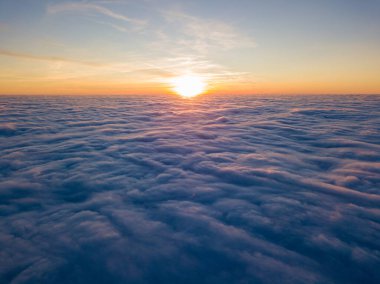 Kıvırcık bulutların üzerinde gün batımı, havada yüksek uçuş. Güneşin son ışınları bulutların üzerinde parlıyor.