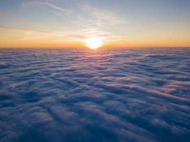 Kıvırcık bulutların üzerinde gün batımı, havada yüksek uçuş. Güneşin son ışınları bulutların üzerinde parlıyor.