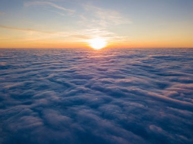 Kıvırcık bulutların üzerinde gün batımı, havada yüksek uçuş. Güneşin son ışınları bulutların üzerinde parlıyor.