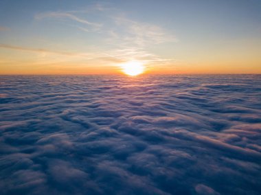 Kıvırcık bulutların üzerinde gün batımı, havada yüksek uçuş. Güneşin son ışınları bulutların üzerinde parlıyor.