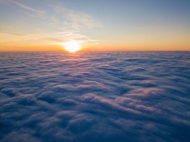 Kıvırcık bulutların üzerinde gün batımı, havada yüksek uçuş. Güneşin son ışınları bulutların üzerinde parlıyor.