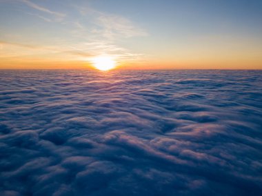 Kıvırcık bulutların üzerinde gün batımı, havada yüksek uçuş. Güneşin son ışınları bulutların üzerinde parlıyor.