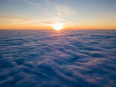 Kıvırcık bulutların üzerinde gün batımı, havada yüksek uçuş. Güneşin son ışınları bulutların üzerinde parlıyor.