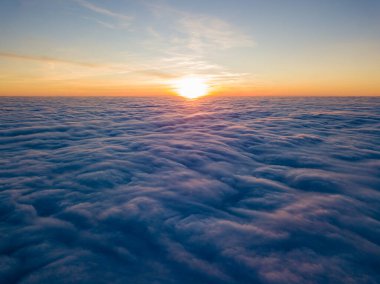 Kıvırcık bulutların üzerinde gün batımı, havada yüksek uçuş. Güneşin son ışınları bulutların üzerinde parlıyor.