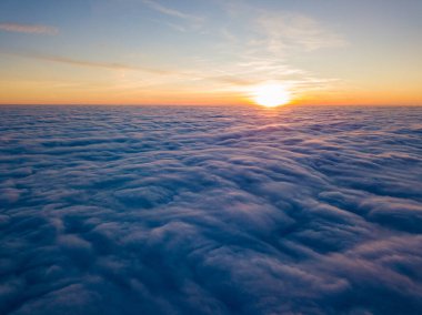 Kıvırcık bulutların üzerinde gün batımı, havada yüksek uçuş. Güneşin son ışınları bulutların üzerinde parlıyor.
