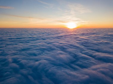 Kıvırcık bulutların üzerinde gün batımı, havada yüksek uçuş. Güneşin son ışınları bulutların üzerinde parlıyor.