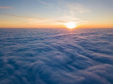 Kıvırcık bulutların üzerinde gün batımı, havada yüksek uçuş. Güneşin son ışınları bulutların üzerinde parlıyor.