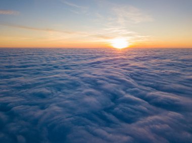 Kıvırcık bulutların üzerinde gün batımı, havada yüksek uçuş. Güneşin son ışınları bulutların üzerinde parlıyor.