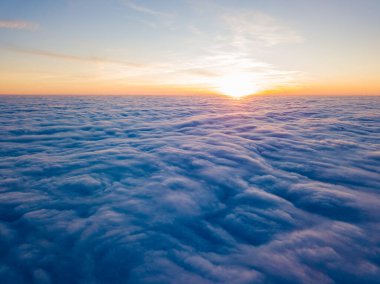Kıvırcık bulutların üzerinde gün batımı, havada yüksek uçuş. Güneşin son ışınları bulutların üzerinde parlıyor.