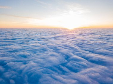 Kıvırcık bulutların üzerinde gün batımı, havada yüksek uçuş. Güneşin son ışınları bulutların üzerinde parlıyor.
