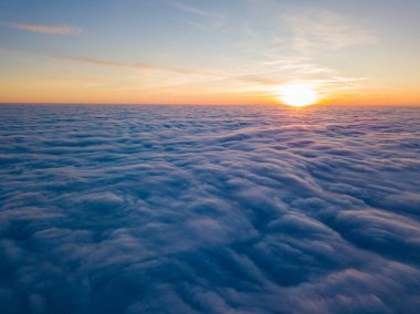 Kıvırcık bulutların üzerinde gün batımı, havada yüksek uçuş. Güneşin son ışınları bulutların üzerinde parlıyor.