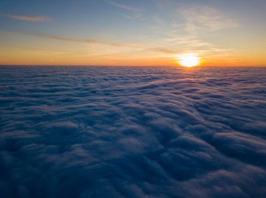 Kıvırcık bulutların üzerinde gün batımı, havada yüksek uçuş. Güneşin son ışınları bulutların üzerinde parlıyor.