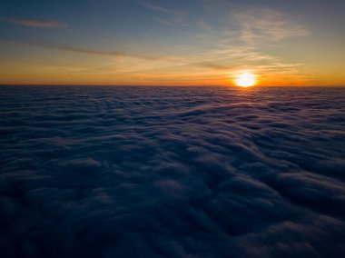 Kıvırcık bulutların üzerinde gün batımı, havada yüksek uçuş. Güneşin son ışınları bulutların üzerinde parlıyor.
