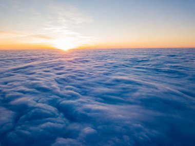 Kıvırcık bulutların üzerinde gün batımı, havada yüksek uçuş. Güneşin son ışınları bulutların üzerinde parlıyor.