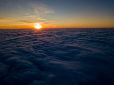 Kıvırcık bulutların üzerinde gün batımı, havada yüksek uçuş. Güneşin son ışınları bulutların üzerinde parlıyor.