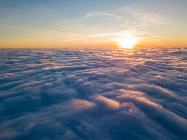 Kıvırcık bulutların üzerinde gün batımı, havada yüksek uçuş. Güneşin son ışınları bulutların üzerinde parlıyor.