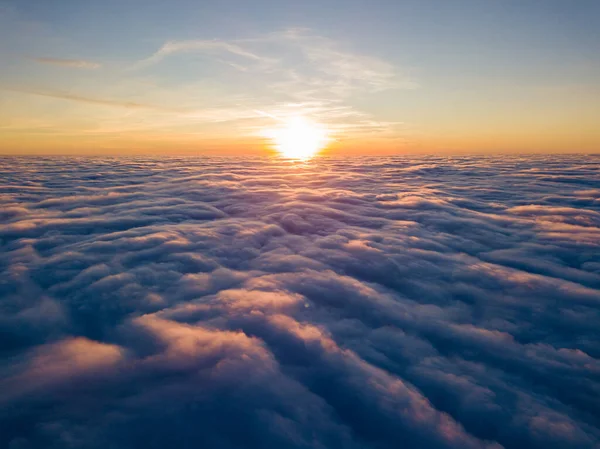 Kıvırcık bulutların üzerinde gün batımı, havada yüksek uçuş. Güneşin son ışınları bulutların üzerinde parlıyor.