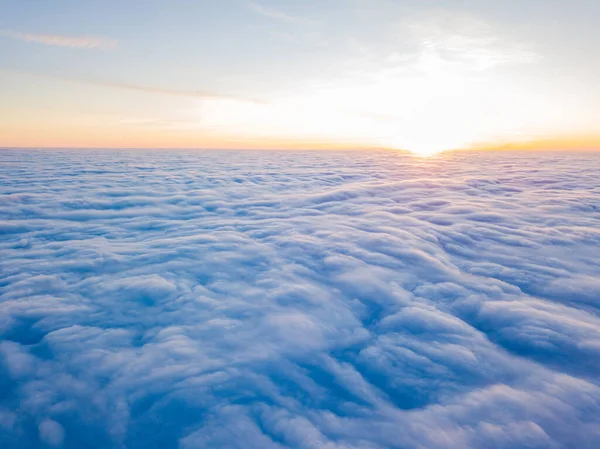 Kıvırcık bulutların üzerinde gün batımı, havada yüksek uçuş. Güneşin son ışınları bulutların üzerinde parlıyor.