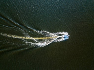 Hava aracı görüntüsü. Güneşli bir yaz gününde nehirdeki bir teknenin arkasında sörf yaparak uyanmak.