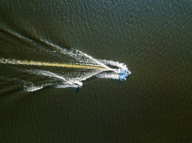 Hava aracı görüntüsü. Güneşli bir yaz gününde nehirdeki bir teknenin arkasında sörf yaparak uyanmak.