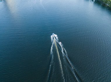 Hava aracı görüntüsü. Güneşli bir yaz gününde nehirdeki bir teknenin arkasında sörf yaparak uyanmak.