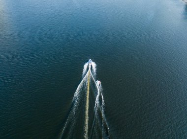 Hava aracı görüntüsü. Güneşli bir yaz gününde nehirdeki bir teknenin arkasında sörf yaparak uyanmak.