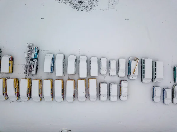 Snow-covered emergency special vehicles in the parking lot. Snowy day, blizzard. Aerial drone view.