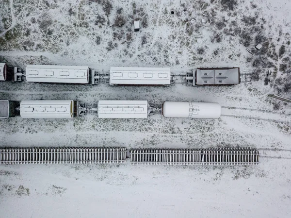 Snow-covered freight train at the station. Snowy day, blizzard. Aerial drone view.