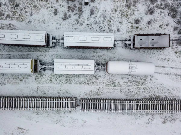 Snow-covered freight train at the station. Snowy day, blizzard. Aerial drone view.