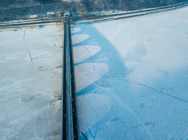 Aerial drone view. The shadow from the metro bridge in Kiev falls on the frozen Dnieper River. Sunny winter morning.
