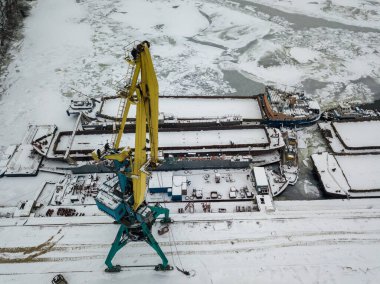 Donmuş bir bölmedeki kargo gemisinin yanında bir vinç. Hava aracı görüntüsü. Kış karlı sabah.
