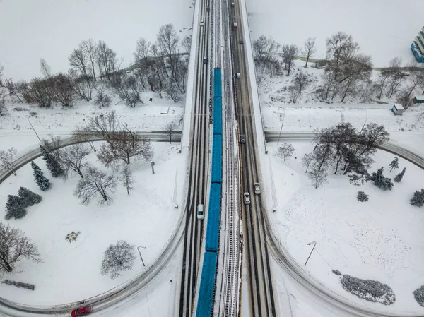 The Kiev metro train passes over a snow-covered bridge. Aerial drone view. Winter snowy morning.