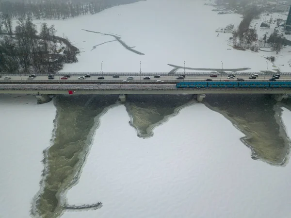 One train on Kiev metro bridge across the frozen Dnieper river. Textured pattern on ice. Aerial drone view. Winter frosty morning.